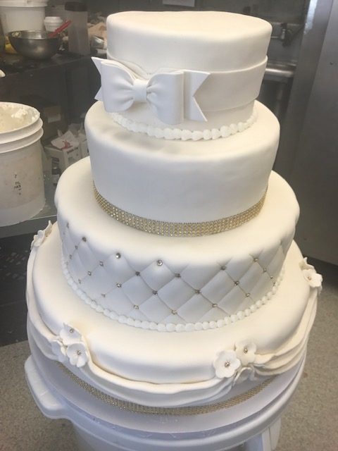 Layered white cake decorated with a bow, flowers and crystals